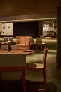 昏黃燈光下的餐廳用餐區，中央擺放大型木桌與金屬椅，四周散落盤碗與花瓶，營造溫暖且親切的氛圍