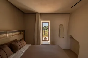 A dimly lit bedroom with a bed, window, and mirror, featuring a bed frame, window frame, and mirror frame, with neutral colors and soft warm lighting