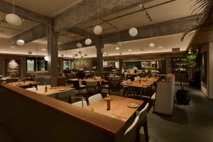 A dimly lit restaurant with wooden floor, empty tables and chairs, and a warm atmosphere