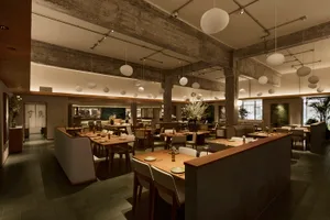 Spacious modern Japanese restaurant interior featuring exposed concrete ceiling beams, numerous spherical pendant lights, wooden dining tables, and upholstered seating arranged in multiple zones.