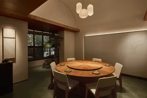 Modern minimalist dining room with a large round oak table, six upholstered chairs, curved wooden ceiling detail, and textured wall with topographic lines.