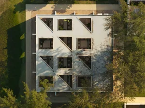 Aerial photograph of an architectural model of a white concrete house with multiple triangular and square courtyards surrounded by greenery.