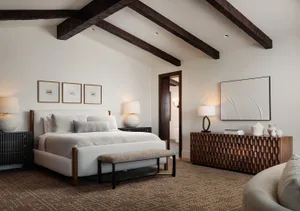 Modern rustic bedroom with white walls, exposed dark wooden ceiling beams, upholstered bed with neutral linens, textured wooden console, and herringbone carpet.
