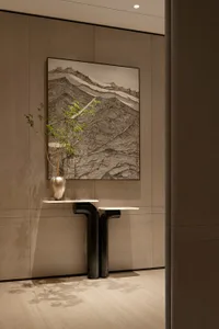 Modern minimalist entryway featuring a sculptural black console table, white marble top, metallic vase with greenery, and a large framed Chinese ink mountain painting against warm walnut paneling.