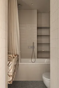 Modern minimalist bathroom with beige fluted wall tiles, built-in white bathtub, marble vanity, white toilet, and beige shower curtain.