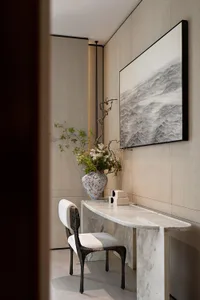 Minimalist entryway featuring a curved white marble console table, a dark sculptural chair, a large ceramic vase with floral arrangement, and a black-framed ink wash painting of waves on a light wood-paneled wall.