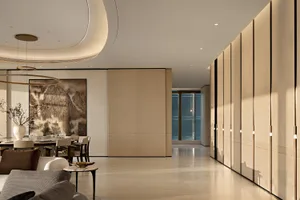 Modern open-plan dining and living space featuring a large circular chandelier, neutral upholstered seating, a round dining table, and a prominent black-and-white mountain ink painting on a vertically ribbed wall, complemented by warm oak paneling and a glossy light floor.