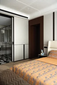 Modern luxury bedroom interior with dark walnut wood paneling, light textured walls, orange and grey checker-pattern duvet, cream leather headboard, and black-framed glass door leading to an en-suite bathroom.