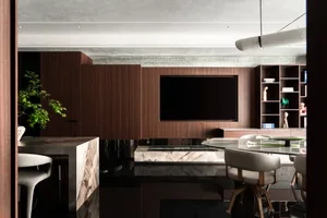 Modern luxury dining room with dark walnut built-in entertainment wall, large wall-mounted TV, marble dining table and light grey upholstered chairs.