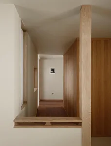 Narrow minimalist hallway featuring light oak wood paneling, built-in floating shelves, and a warm wood floor.