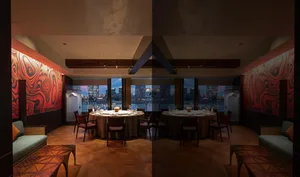 Luxurious private dining room featuring a large round table, red marble accent walls, walnut herringbone flooring, and floor-to-ceiling windows overlooking a harbor city skyline at dusk.