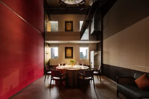 Modern private dining room featuring a bold red lacquer wall, round dining table with six chairs, double-height ceiling, and dark wood accents.