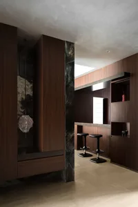 Modern luxury home bar with dark walnut wood cabinetry, green marble wall, sculptural glass pendant light, and two black bar stools in a minimalist interior.