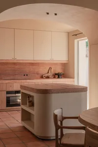 Modern kitchen featuring a curved terracotta kitchen island, matching backsplash, light wood cabinetry, and a large arched plaster ceiling detail with terracotta floor tiles.