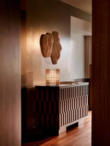 Modern entryway console featuring a dark checkerboard wood pattern, topped with a grid-patterned table lamp and an open book, with two large textured organic wall sculptures mounted on a metallic gold wall.
