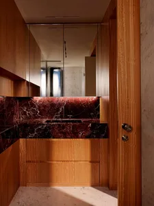 Modern luxury bathroom with warm wood cabinetry, red marble countertop and backsplash, integrated sink, and large mirror.