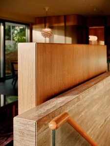 Modern staircase featuring a thick travertine stone balustrade, a wooden handrail, and a warm oak wood partition wall in the background.