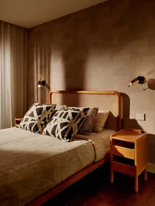 Modern bedroom featuring a wooden bed with a large rattan cane headboard, black and white geometric pillows, wooden nightstand, and patterned wood wall with wall sconces.
