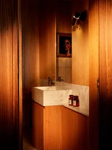 Modern powder room featuring a white marble rectangular vessel sink, walnut wood cabinetry, marble backsplash, and a framed portrait reflected in the mirror under warm wall sconce lighting.