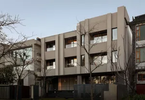 Modern multi-story concrete residential building with large glass windows and cantilevered glass balconies, surrounded by leafless trees at dusk.