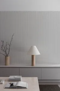 Modern minimalist living room featuring a white fluted wall, grey floating console, travertine table lamp with fabric shade, and a travertine coffee table with open books and a wooden vase with dried branches.