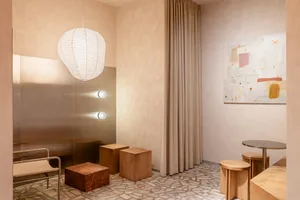 Modern minimalist lounge corner featuring a large white paper lantern, beige textured walls, stone terrazzo floor, wooden cube stools, and an abstract painting.