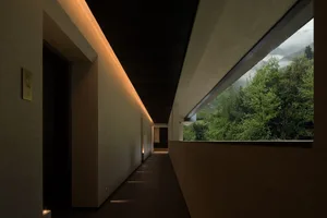 長長的現代混凝土走廊，配有溫暖線性照明，大型開口外可見霧氣繚繞的蒼翠山景。