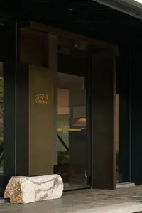 Modern entrance featuring a large natural travertine boulder at the base of a dark bronze and wood doorway with gold Chinese characters reading Yunxigu.