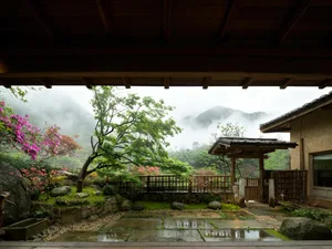 Traditional Japanese courtyard garden with stone pavers, moss, blooming azaleas, wooden fence, and misty green mountains in the background, viewed from a wooden veranda.