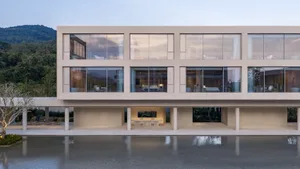 Modern concrete luxury villa with extensive glass walls and a large reflecting pool in front, set against a forested mountain backdrop at dusk.