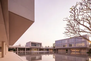 Modern minimalist concrete villa with large glass windows, elevated on pillars, surrounding a large rectangular reflecting pool at dusk, with a plumeria tree in the foreground.