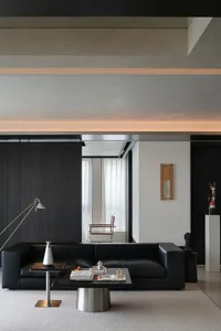 Modern minimalist living room featuring exposed concrete ceiling, black leather sofa, dark wood wall paneling, and sculptural lighting.