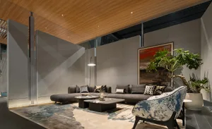 Modern living room with grey L-shaped sectional sofa, blue and white patterned accent chair, concrete walls, wooden ceiling, and large potted plant.
