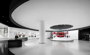 Modern white exhibition hall with dramatic curved black ceiling, glossy white floor, central white column, and a red Mercedes-Benz car displayed in exploded view on a circular platform.