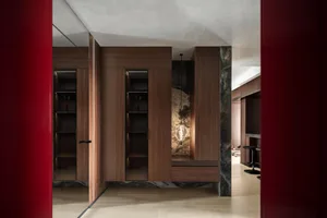 Modern luxury entryway featuring rich walnut built-in cabinetry, dark marble accents, glossy red lacquer doors, and a hand-blown glass pendant light.