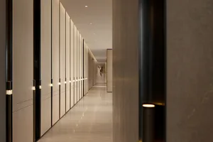Long modern hallway featuring floor-to-ceiling light wood paneling with integrated vertical LED lighting and polished stone flooring.