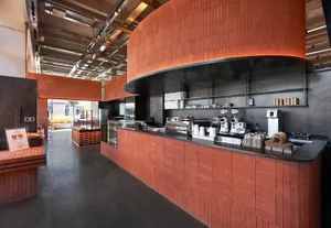 Modern café interior featuring a long curved service counter finished in terracotta tiles, dark concrete floor, and dramatic overhead lighting.