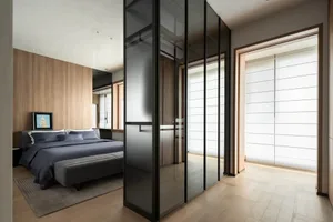 Contemporary bedroom interior with walnut wood accent wall, dark blue bedding, glass wardrobe with black metal frames, and a grey upholstered bench at the foot of the bed.