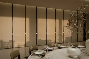 Elegant modern dining room with a round white marble table set for dinner, taupe leather chairs, and a dramatic floor-to-ceiling backlit oak panel wall with vertical light accents.