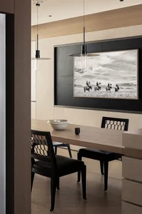 Modern dining room featuring a light oak table, black lattice-back chairs, two black pendant lights, and a large black-and-white photograph of cowboys on horseback.