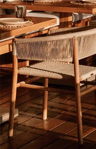A wooden dining chair with beige rope weaving on the backrest and seat, placed on a dark wooden deck beside a solid wood dining table.