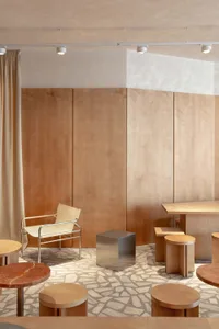 Modern lounge area featuring light wood panel walls, a chrome and leather chair, stainless steel cube, round wooden stools, and a distinctive fragmented stone terrazzo floor.