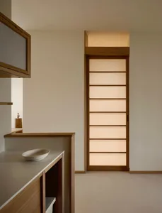 極簡風室內空間，畫面中央為直立式橡木拉門，門上有水平半透光面板並由後方暖光照亮，前景有木質檯面與白色碗。