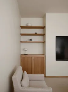 Minimalist living room corner with light oak cabinet, three floating oak shelves, white walls, and a cream fabric sofa in the foreground.