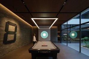 Modern minimalist billiard room with dark stone accent wall, black pool table, large square LED light fixture, and glowing cyan spherical pendant lights.