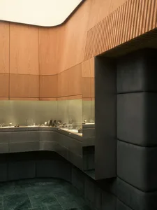 Interior view of a luxury jewelry store featuring curved walnut wood paneling, backlit glass display cases, and dark green marble tile flooring with padded dark wall panels.