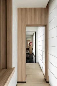 Modern minimalist hallway with light wood paneling, white textured walls, and a red stone sculpture displayed on a pedestal at the end of the corridor.