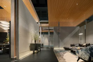 Modern open-plan living room featuring a dramatic double-height wood ceiling, concrete partition walls, dark tiled floor, and contemporary furniture with a patterned armchair in the foreground.