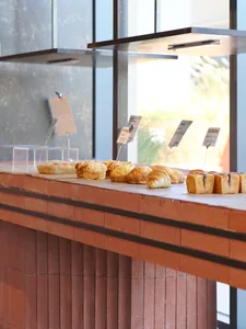 A bakery pastry counter made of terracotta tiles displaying various fresh pastries including croissants and buns under modern overhead lighting with large windows in the background.