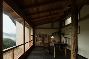 Interior of a mountain villa dining room featuring solid wood furniture, exposed timber ceiling beams, and large windows revealing a misty forest landscape.